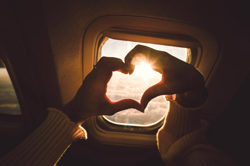 Tourist woman making heart shape with hands in airplane - Travel